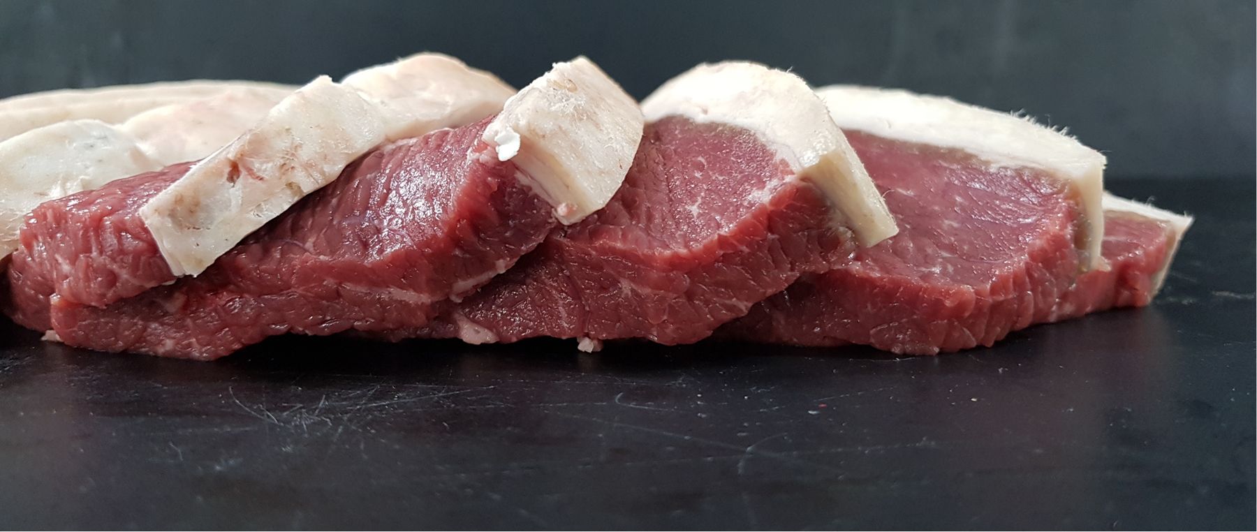 Dry aged rump steak, sliced, on a dark board