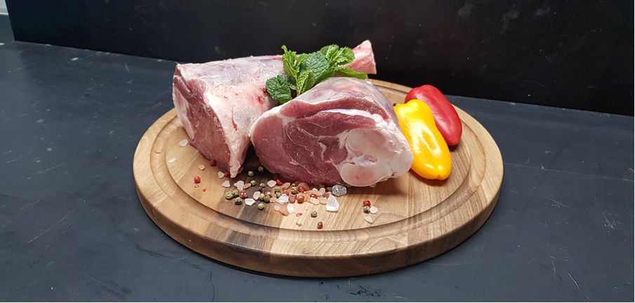 Lamb shoulder on a round wooden board with peppers and herbs